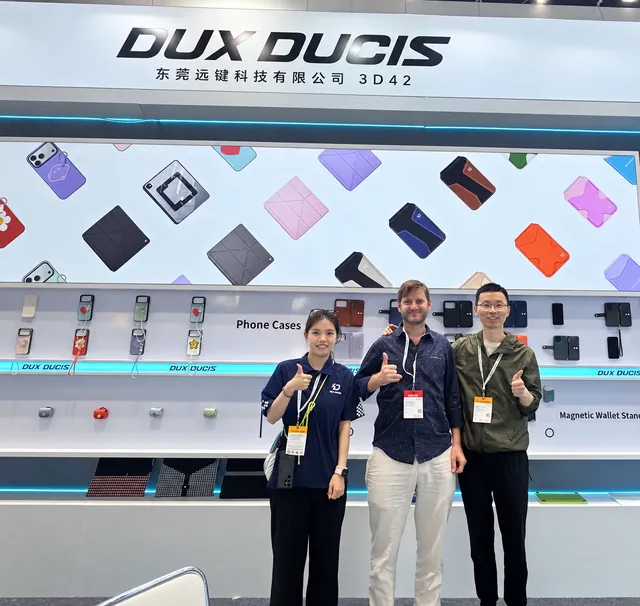 Tres personas posando frente al expositor de fundas para móviles de DUX DUCIS