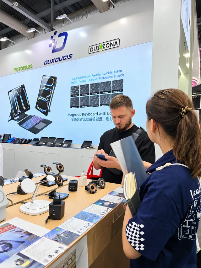 Un visitante y un miembro del equipo de DUX DUCIS hablando sobre productos en el mostrador de la feria